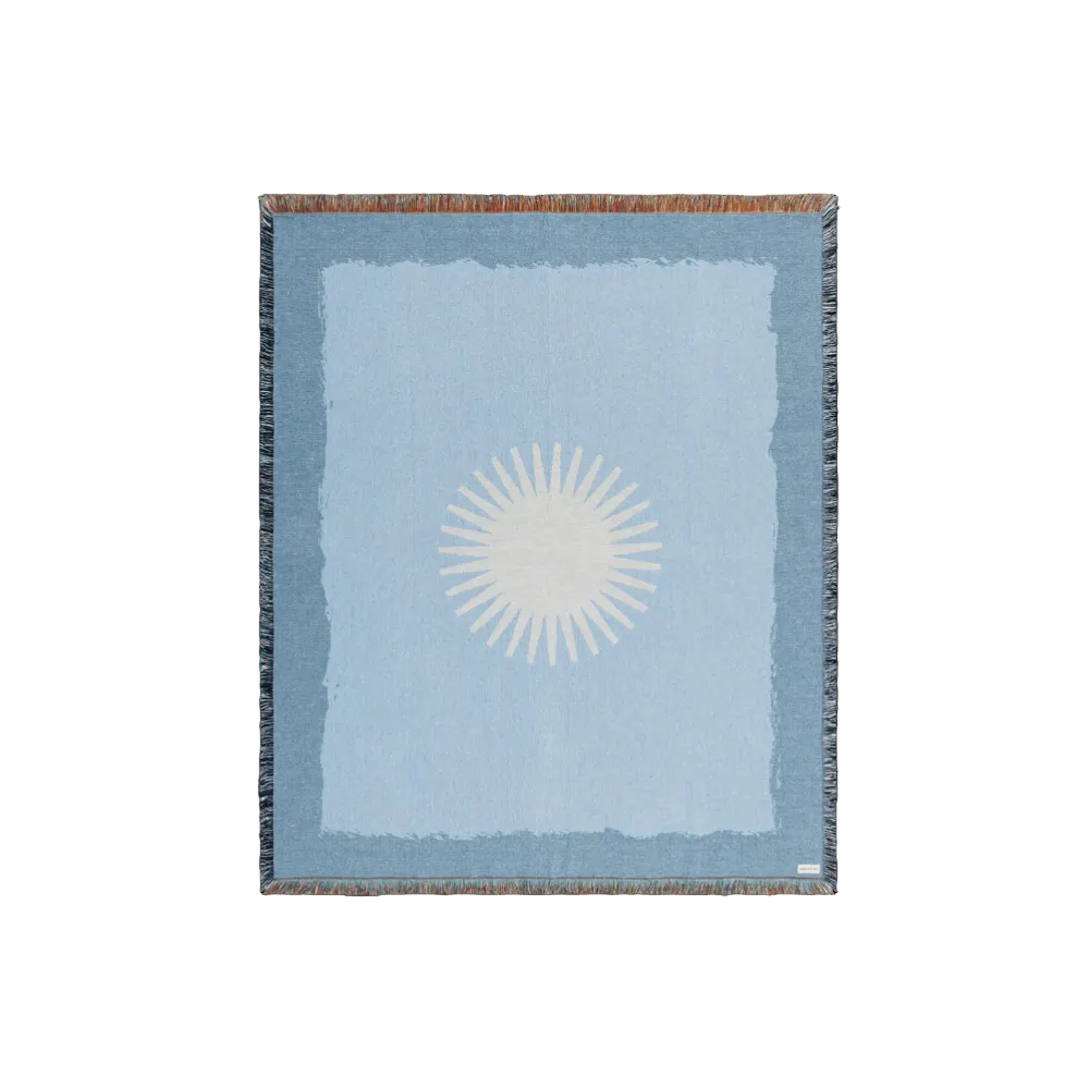 Lichtblauwe deken met wit zonnesymbool en blauwe franjerand, close-up.