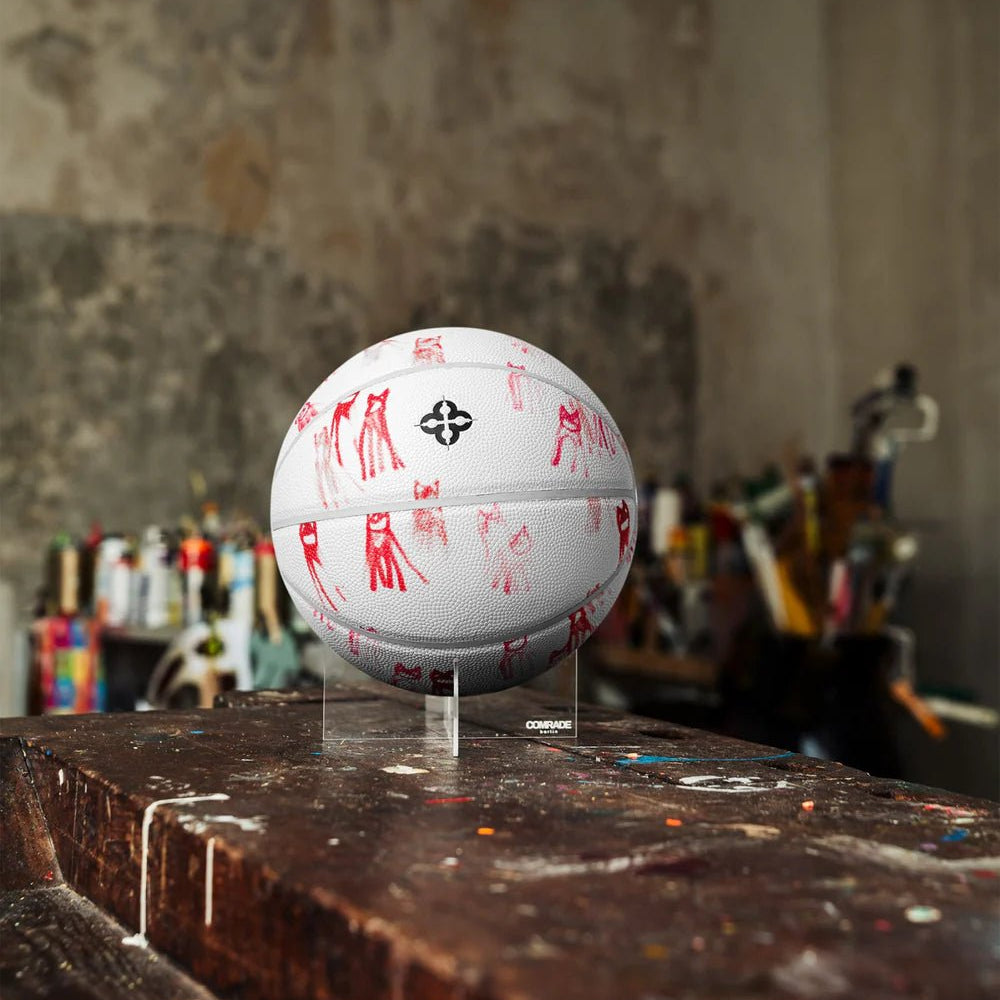 Witte basketbal met rode prints en zwart klaver-embleem op plank
